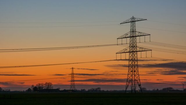 Silhouette of high voltage lines against a vibrant sunset sky in the countryside.