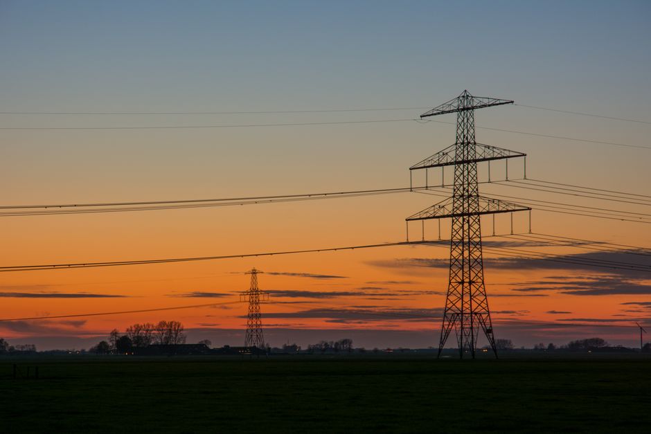 Silhouette of high voltage lines against a vibrant sunset sky in the countryside.