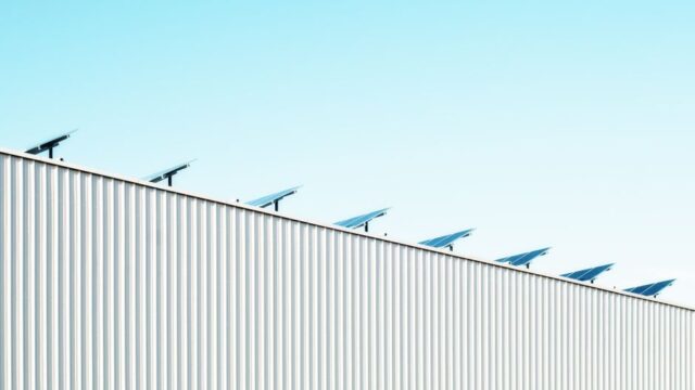 Corrugated steel building with solar panels under a clear blue sky, emphasizing sustainability.