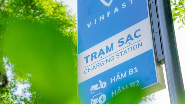 Close-up of a VinFast charging station sign with green leaves in the foreground, indicating eco-friendly technology.