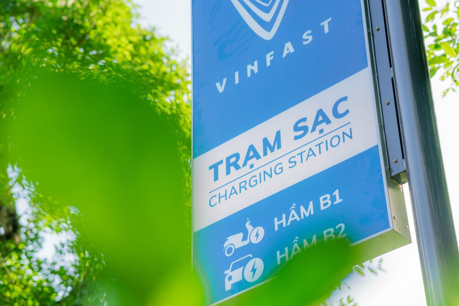 Close-up of a VinFast charging station sign with green leaves in the foreground, indicating eco-friendly technology.