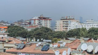 Urban cityscape featuring rooftops with solar panels and satellite dishes surrounded by buildings and trees.