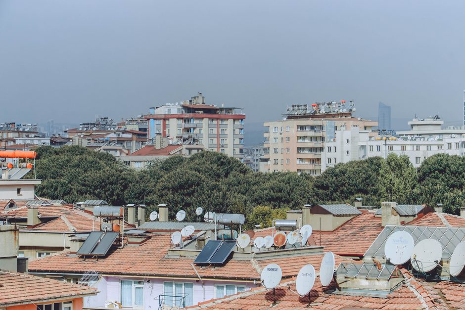 Urban cityscape featuring rooftops with solar panels and satellite dishes surrounded by buildings and trees.