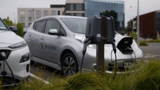 Electric vehicles at a charging station in Christchurch parking lot with modern architecture.