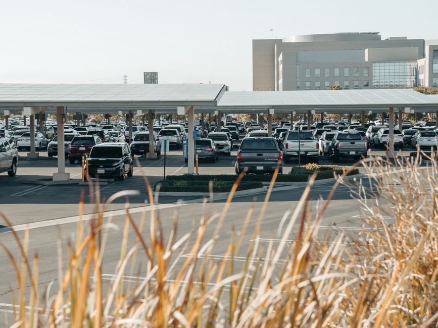A large parking lot with solar panels covering parked cars at a commercial building.