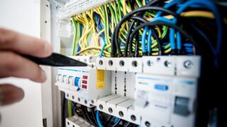Hand of electrician working on a circuit breaker panel with colorful wires, ensuring safe electrical connections.