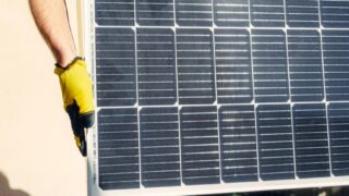 Close-up of a person installing a solar panel outdoors under bright sunlight.