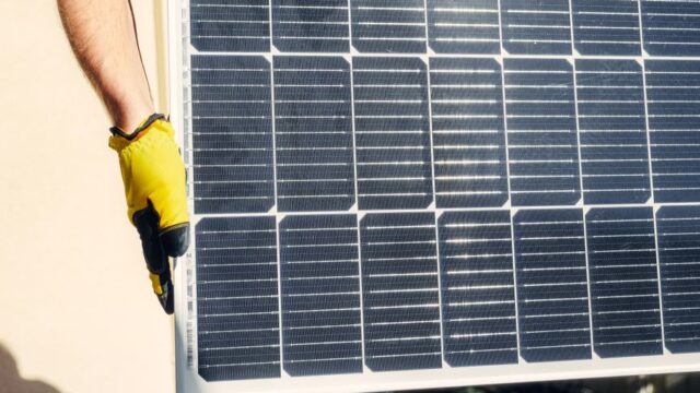 Close-up of a person installing a solar panel outdoors under bright sunlight.