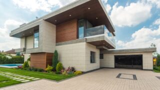 Contemporary luxury house with a sleek design, lush garden, and blue sky.