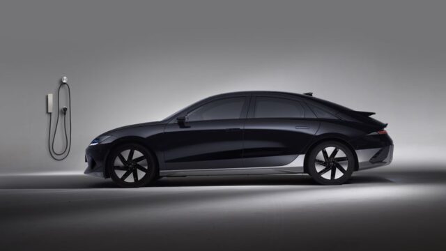 Side view of a black electric car in a studio, showcasing sleek design and charging station.