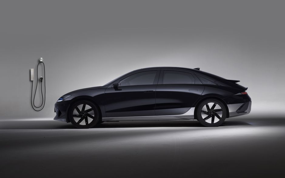 Side view of a black electric car in a studio, showcasing sleek design and charging station.