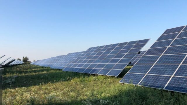 Solar panels in a green field under a clear blue sky in Tortona, Italy.