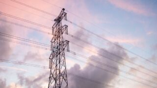 High voltage power lines silhouetted against a vivid sunset sky with clouds.