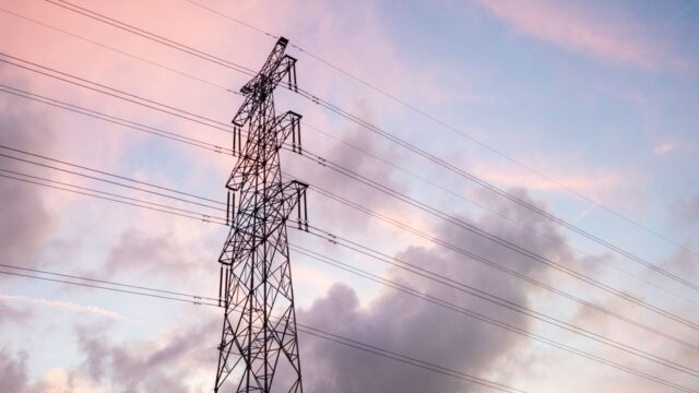 High voltage power lines silhouetted against a vivid sunset sky with clouds.