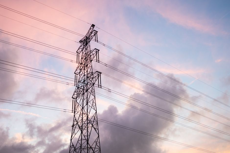 High voltage power lines silhouetted against a vivid sunset sky with clouds.