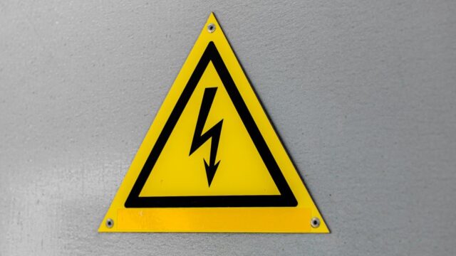 Close-up of a yellow high voltage warning sign mounted on a wall.