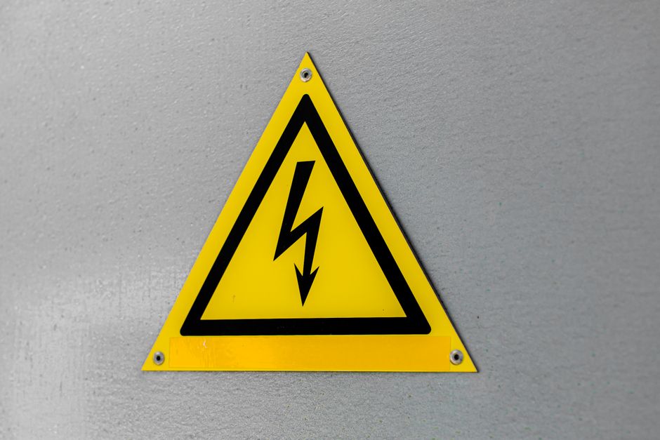 Close-up of a yellow high voltage warning sign mounted on a wall.