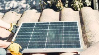 Technician fitting solar panel on rooftop in sunlight. Renewable energy installation.