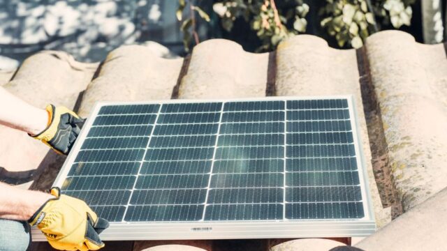 Technician fitting solar panel on rooftop in sunlight. Renewable energy installation.