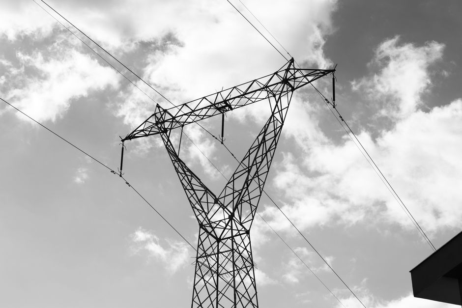A high voltage power line towering against a dramatic cloudy sky in a black and white composition.
