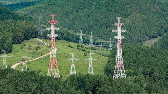 High voltage transmission towers stretching through lush green forest hills, showcasing energy infrastructure.