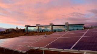Solar panels in front of a modern building at sunset showcasing renewable energy technology.