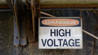 Rusty 'Danger High Voltage' sign on an outdoor wall, indicating electrical hazard.