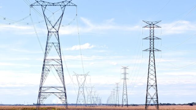 High voltage pylons stretching across a vast open field under a clear blue sky.