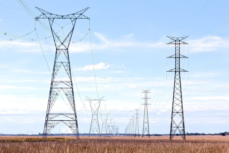 High voltage pylons stretching across a vast open field under a clear blue sky.