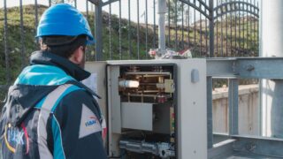 A professional electrician wearing a hard hat inspects an outdoor fuse box ensuring safety.