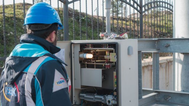A professional electrician wearing a hard hat inspects an outdoor fuse box ensuring safety.