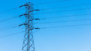 A high voltage transmission tower with power lines under a bright blue sky, showcasing infrastructure.