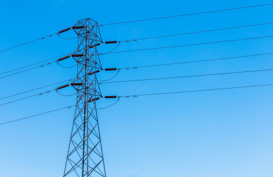 A high voltage transmission tower with power lines under a bright blue sky, showcasing infrastructure.