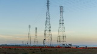 High voltage transmission towers with clear blue sky at dusk in an open field.