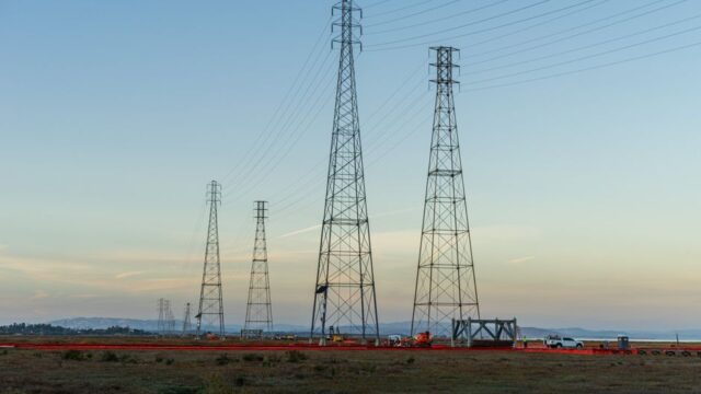 High voltage transmission towers with clear blue sky at dusk in an open field.