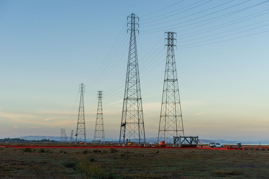 High voltage transmission towers with clear blue sky at dusk in an open field.