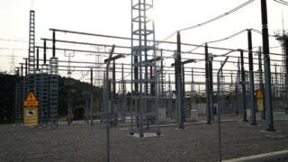 Outdoor electrical power substation with high voltage equipment and safety signs, surrounded by fencing.