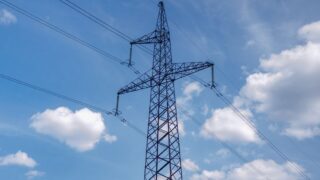 A high voltage transmission tower set against a bright blue sky with scattered clouds, showcasing modern infrastructure.