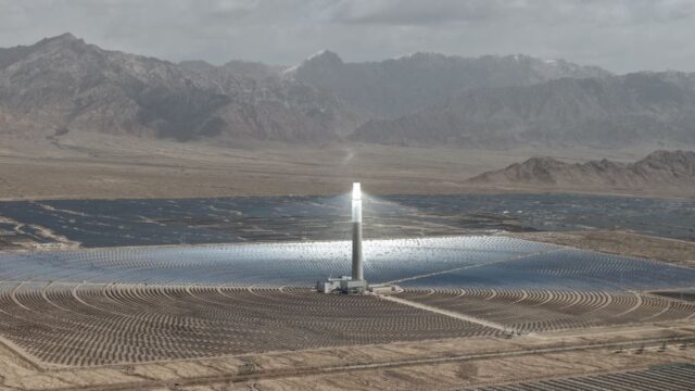 Expansive solar power plant with central tower set against mountain backdrop in Xinjiang desert.