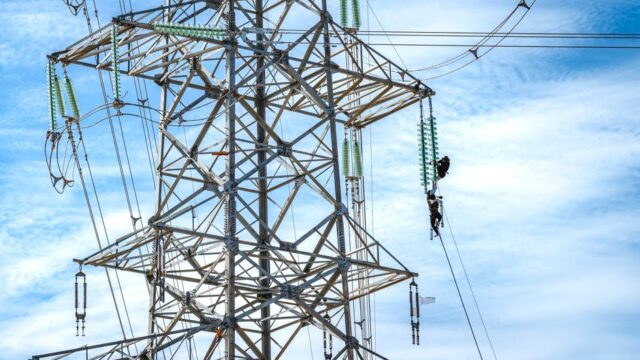 Workers performing maintenance on a high voltage power line against a blue sky.
