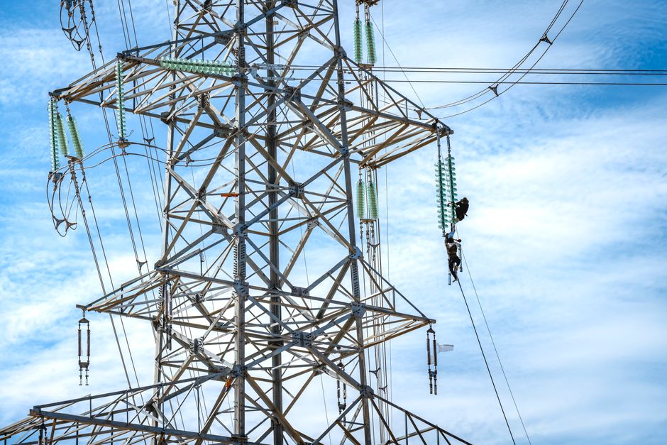 Workers performing maintenance on a high voltage power line against a blue sky.