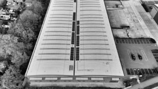 Black and white aerial view of a warehouse in Hertfordshire with solar panels and parking area.
