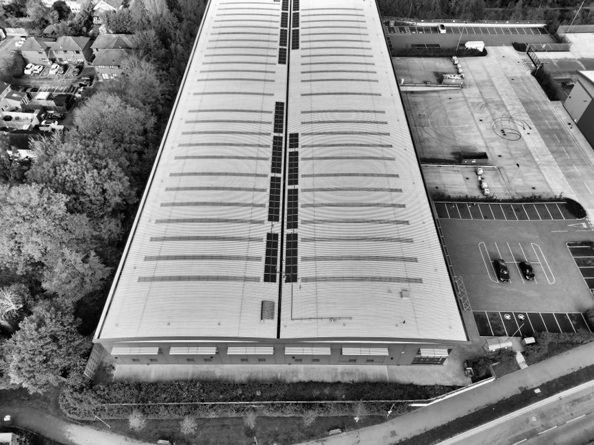 Black and white aerial view of a warehouse in Hertfordshire with solar panels and parking area.
