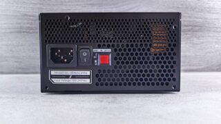 Detailed view of a computer power supply unit back panel with power socket, switch, and ventilation grill.