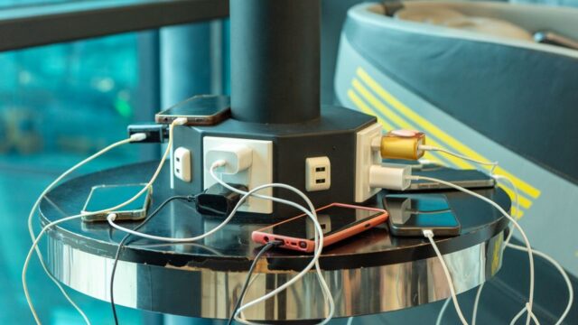 Multiple smartphones charging at a public charging station indoors. USB and electric connections visible.