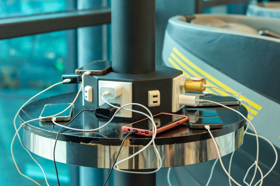 Multiple smartphones charging at a public charging station indoors. USB and electric connections visible.