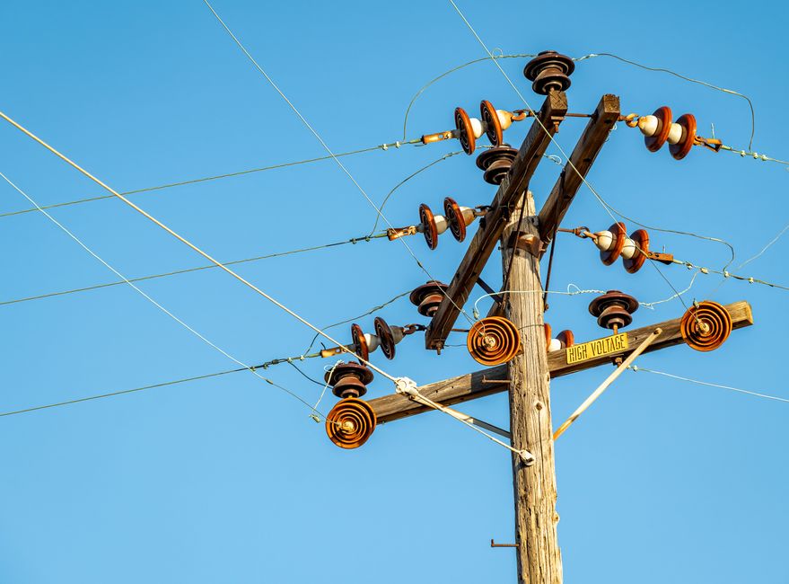 High voltage power line and insulators captured against a clear blue sky.