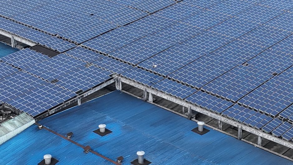 Aerial shot of solar panels installed on a blue industrial rooftop.
