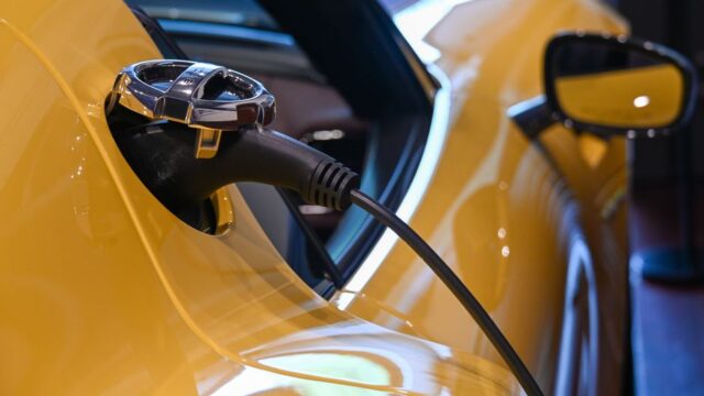 Close-up of a yellow electric vehicle charging with a plugged-in cable indoors.