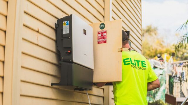 Electrician from Elite Power Group installing a solar inverter outside.